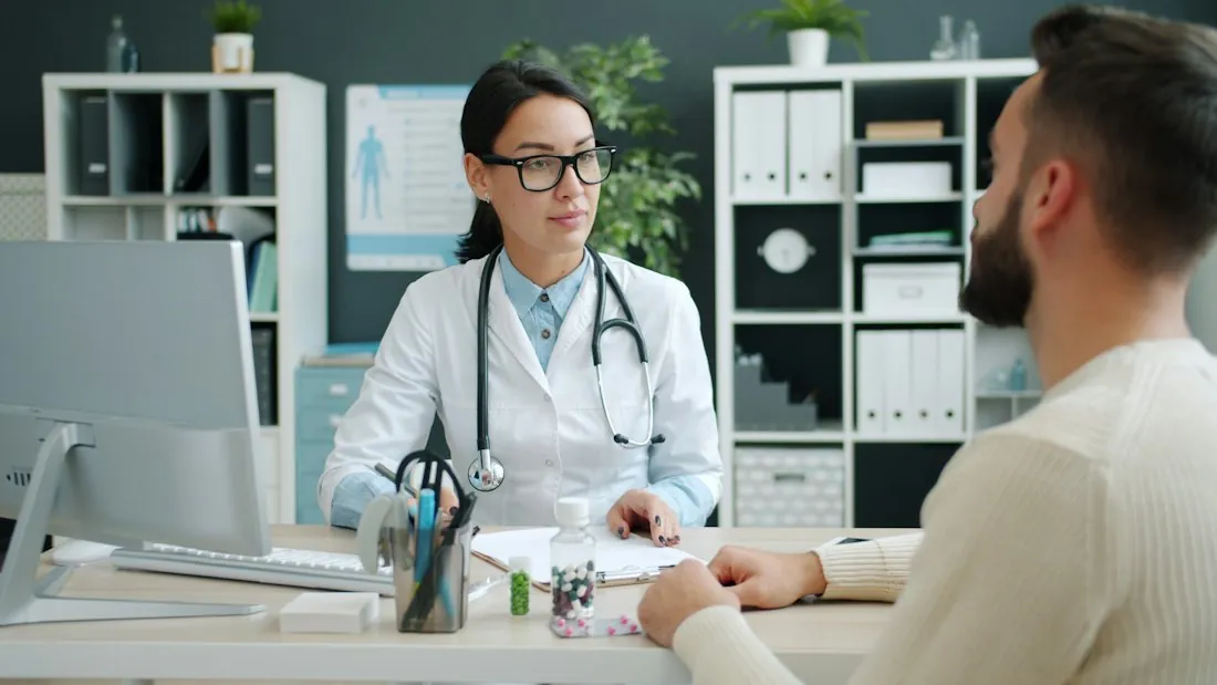 A smiling doctor in a white coat at her desk in a consulting room