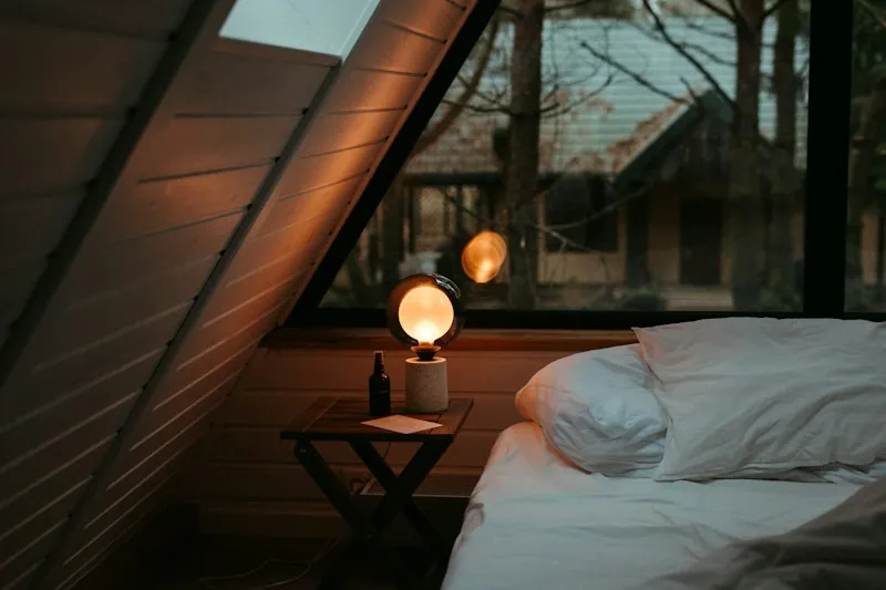 A neatly made bed beneath a window next to a nightstand