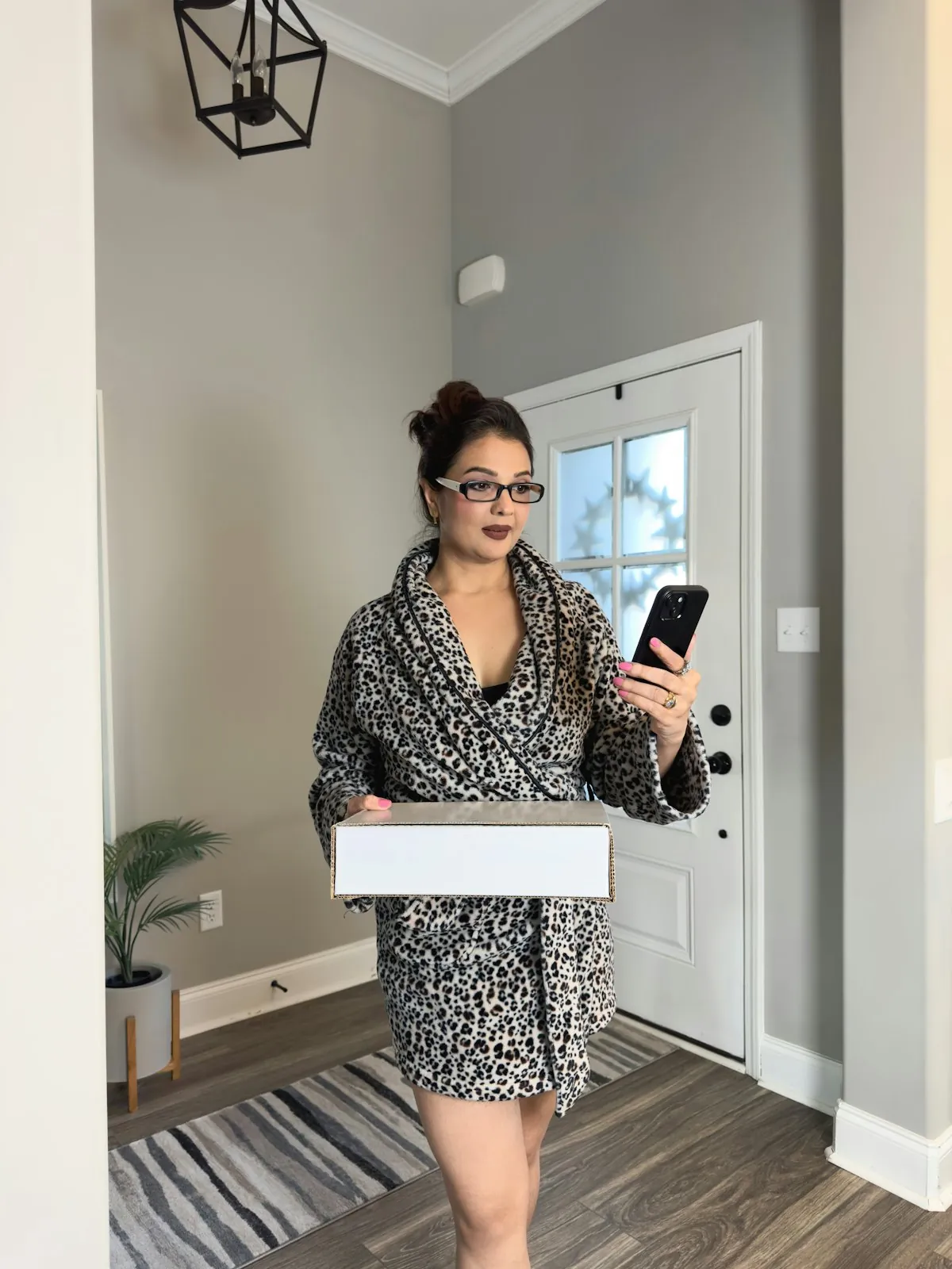 A woman in a robe at her front door holding a delivered parcel